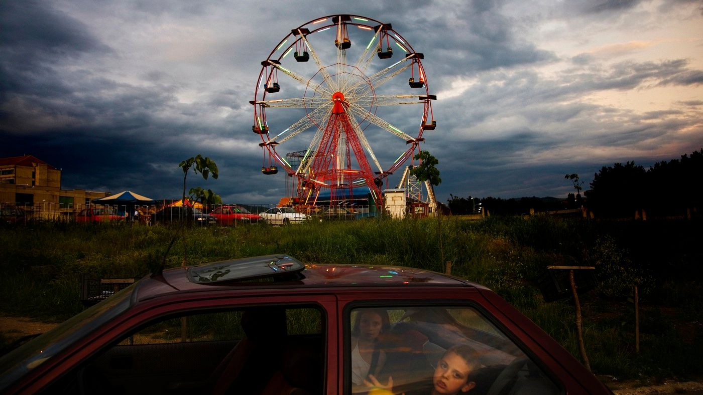 Foreground: kids in the back of a car. Background: Ferris wheel in front of a stormy sky.