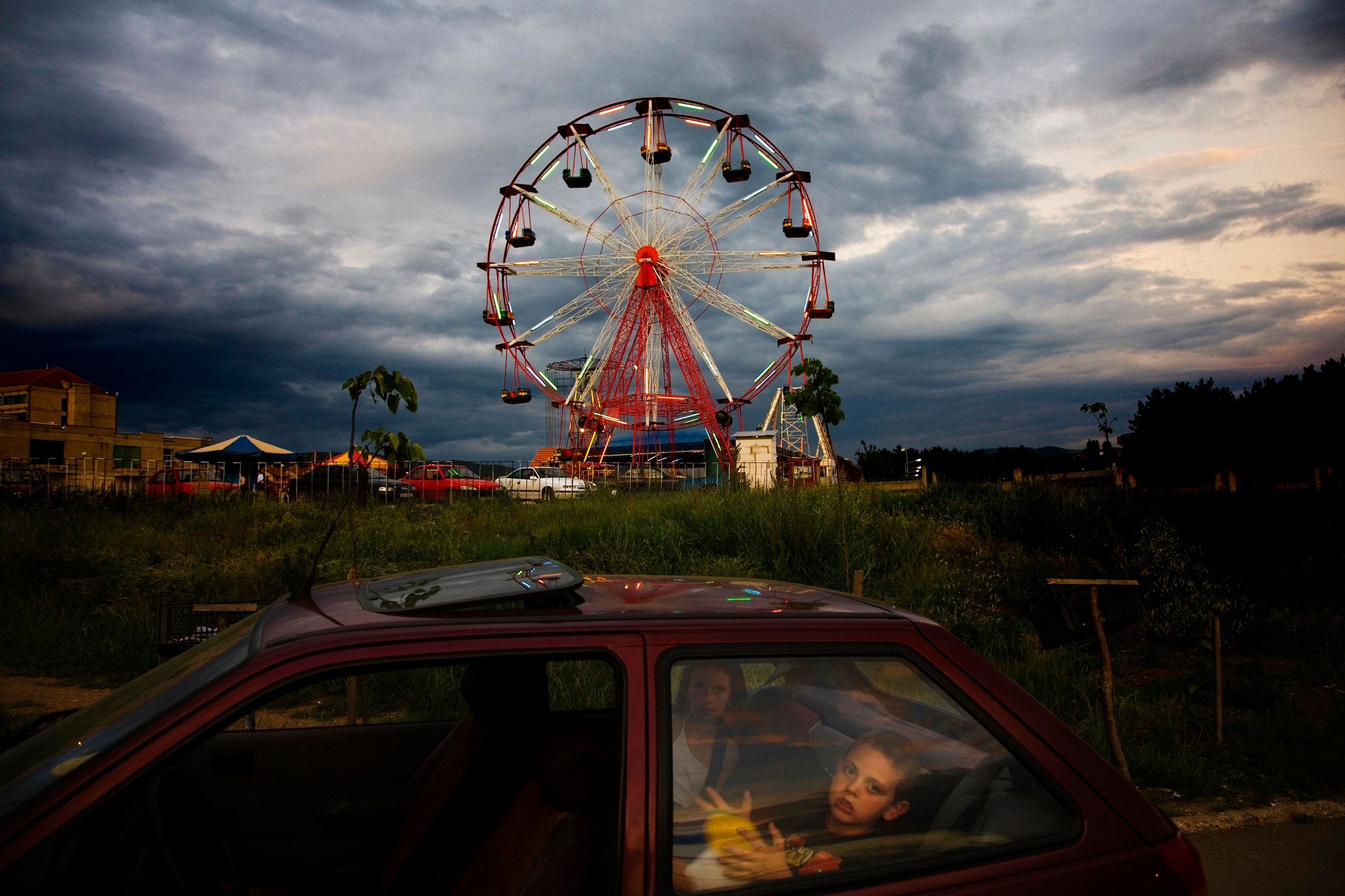 Foreground: kids in the back of a car. Background: Ferris wheel in front of a stormy sky.